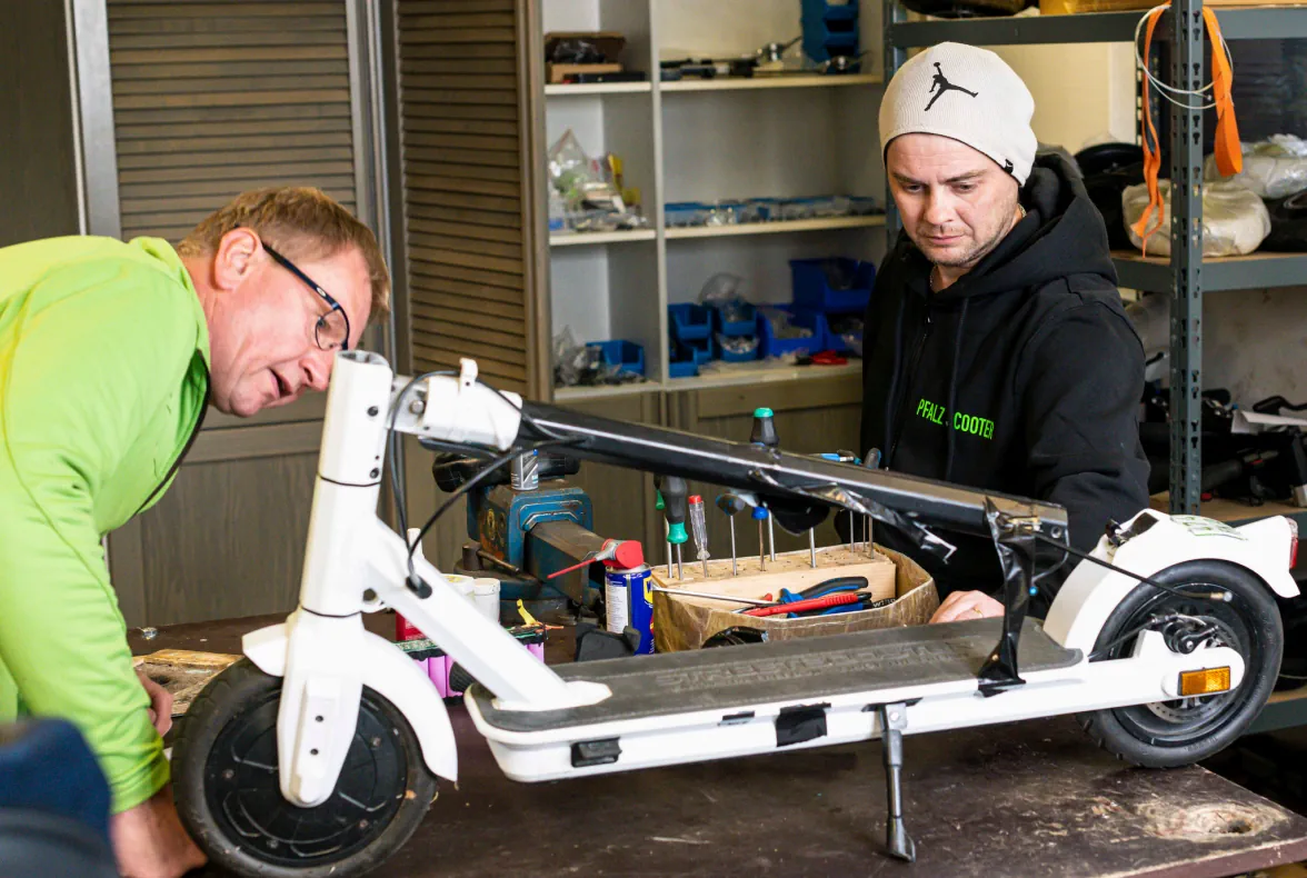 Zwei Techniker reparieren einen weißen E-Scooter